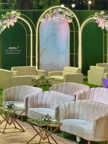A chic lounge area with modern pink and beige sofas, set against a backdrop of green hedge walls and illuminated arches.