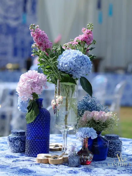 A centerpiece arrangement with pink and blue hydrangeas in cobalt blue vases, set on a beautiful blue and white floral tablecloth.