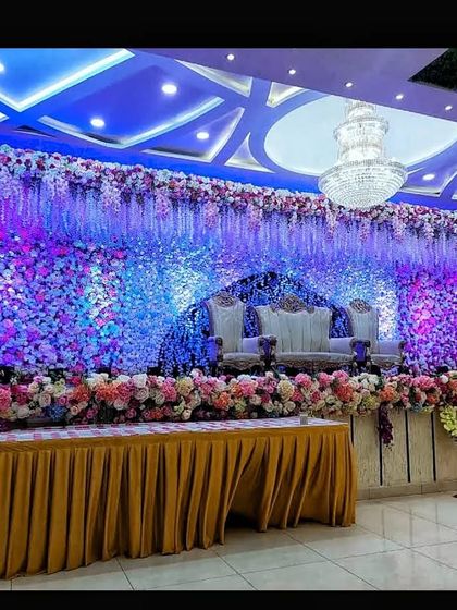A magnificent stage at Akshata banquet hall completely covered in a wall of flowers under dramatic blue and purple lighting. This is perfect for clients who want a truly grand floral backdrop.