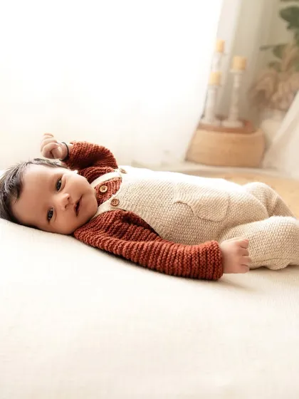A baby boy in a cozy knit outfit, lying on a bed. This lifestyle shot captures a quiet, natural moment at home.