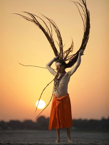 A Naga sadhu with magnificent dreadlocks throws them in the air against the setting sun. This powerful silhouette captures the wild, untamed spirit of asceticism.