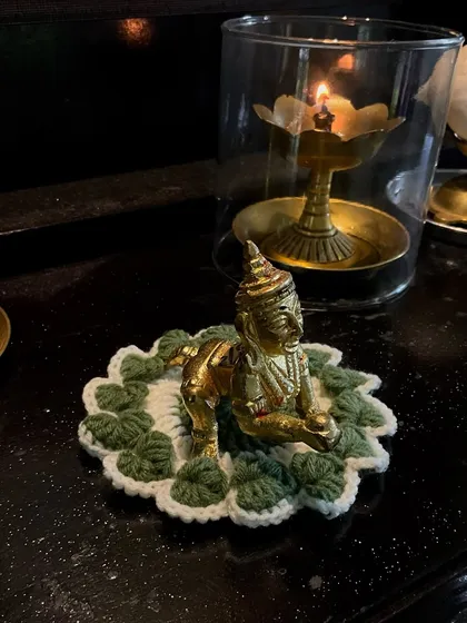A handmade crochet 'asan' or mat for a small Krishna idol. This one in green and white provides a beautiful and respectful seat for the deity in a home temple.