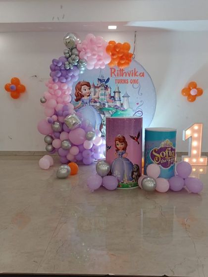 A sweet 'Sofia the First' princess theme for a first birthday. The decoration includes a custom circular backdrop, themed plinths, and a pastel balloon arrangement.