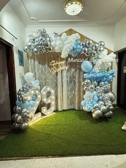 A full view of the 29th birthday decoration. The use of artificial grass on the floor adds an interesting texture to this indoor setup, which includes balloons, marquee numbers, and a neon sign.
