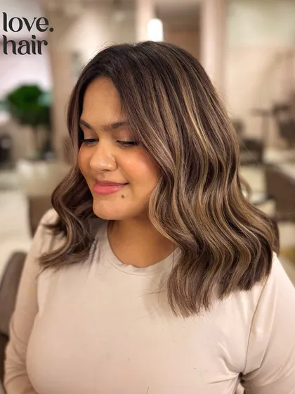 The client smiling with her new ash brown balayage. The color complements her skin tone perfectly, and the wavy bob is effortlessly stylish.