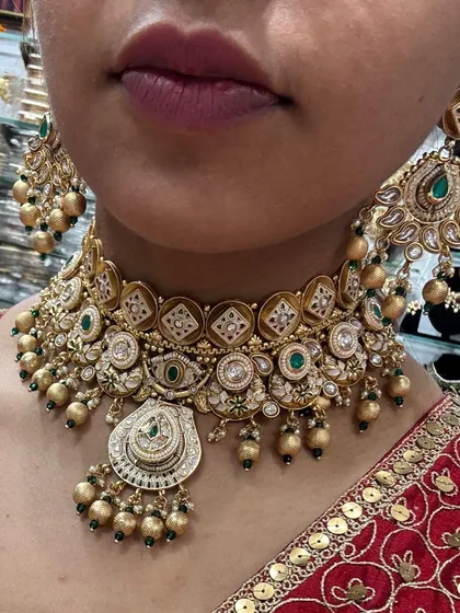 A close-up of a model wearing an antique-finish choker with intricate detailing and green stones, paired with a red embroidered outfit.