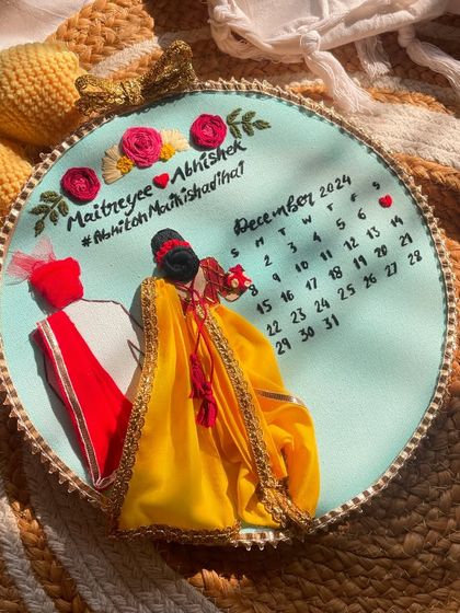 A top-down view of the wedding hoop, showing the embroidered names, hashtag, and the calendar with the special date marked by a heart.