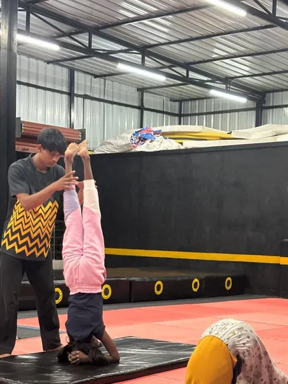 A coach provides support during a headstand to ensure proper form and safety for a young student.