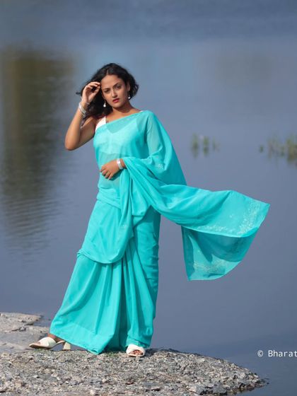 A stunning outdoor portrait by the water. The flowing turquoise saree against the calm blue water creates a beautiful, ethereal image.