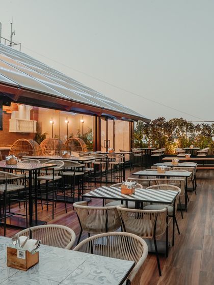 The expansive rooftop terrace is perfect for large groups, with a mix of table sizes and seating arrangements. The glass-roofed section of the restaurant is visible in the background, showing the seamless flow between indoor and outdoor spaces.