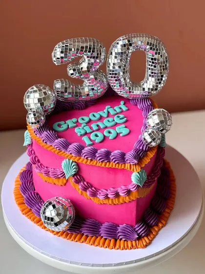 Let's get the party started with a groovy disco-themed cake. This vibrant, heart-shaped cake is perfect for a 30th birthday, featuring disco ball toppers and retro piping for a fun celebration.