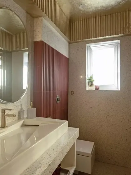 The powder room in the Dumir's project features terrazzo walls, a pop of color with fluted red tiles in the shower area, and a gold-fluted ceiling detail.