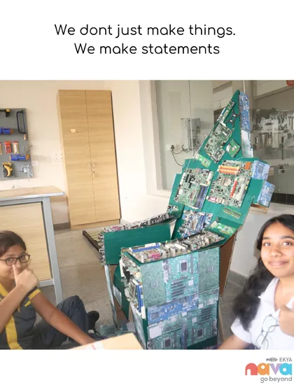 "We don't just make things. We make statements." Two students proudly present a chair they constructed from recycled electronic components, embodying our philosophy of design with purpose and environmental consciousness.