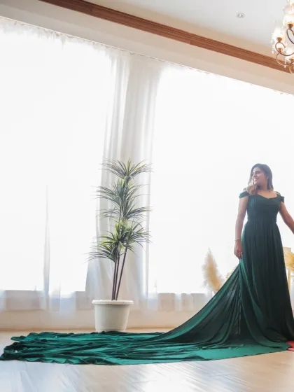 A solo portrait of the bride showcasing her stunning emerald gown with its dramatic train spread out. The bright, natural light from the window creates an ethereal glow.