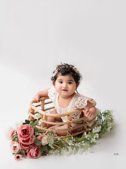 A baby girl sitting in a beautiful rattan basket adorned with pink and white flowers.