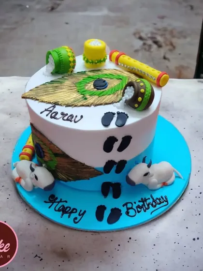 A beautiful Krishna-themed cake for a little one's birthday. It's decorated with peacock feathers, pots of butter, and tiny footprints, capturing the playful spirit of Little Krishna.