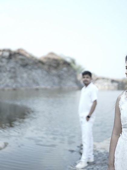 A creative composition with the bride in focus and the groom blurred in the background, set against a scenic lake.