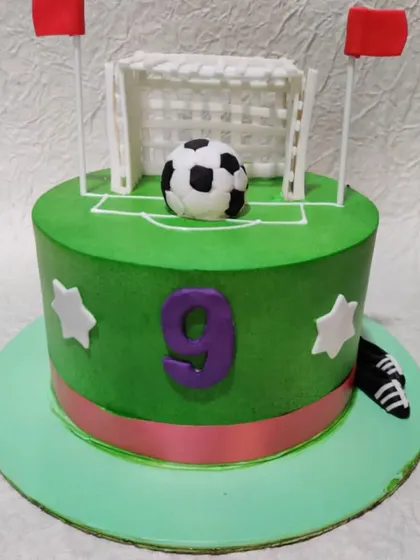 A football-themed cake for a 9th birthday. The cake is designed to look like a soccer field with a goal, a ball, and cleats.