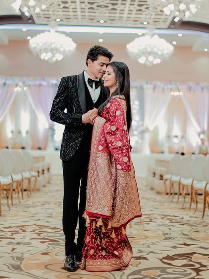 A full-length portrait of the couple in the grand, empty ballroom before their reception. The stunning chandeliers and their elegant attire create a fairytale image.