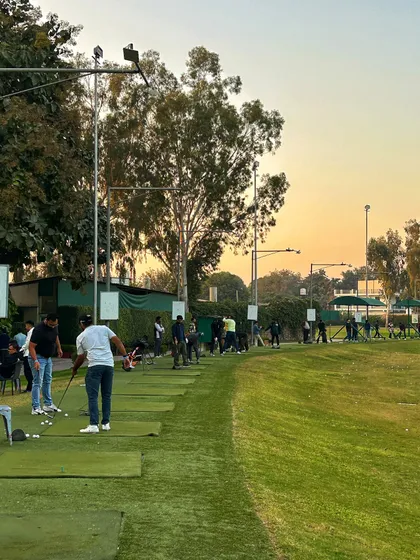 The range is packed as evening approaches, with golfers enjoying the golden hour light.