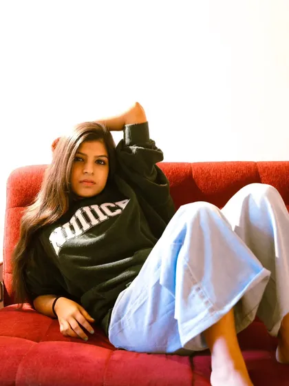 A casual, full-length pose on a bright red sofa. The contrast of the relaxed outfit and the bold furniture is fun and eye-catching.