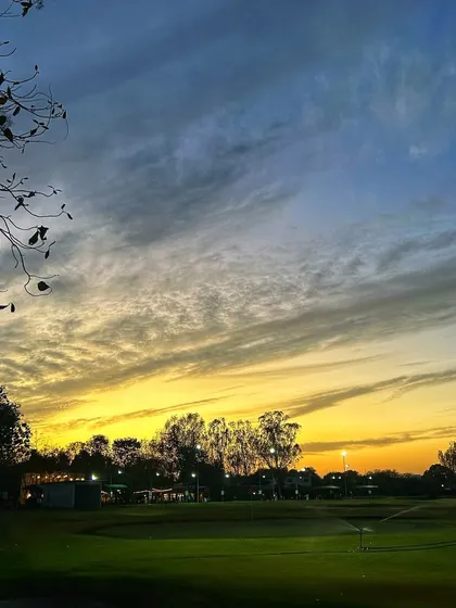 A dramatic sunset paints the sky with streaks of yellow and blue over the driving range.