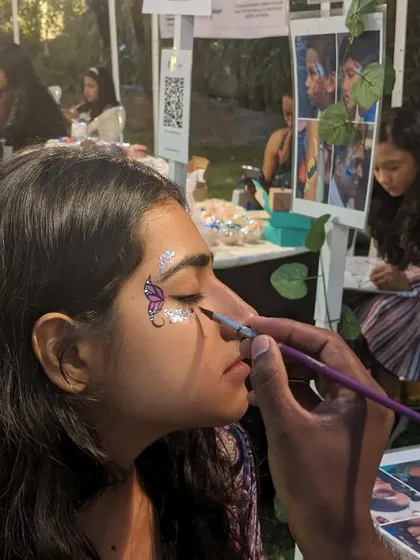 A client getting a purple butterfly with silver glitter applied at an evening market event.