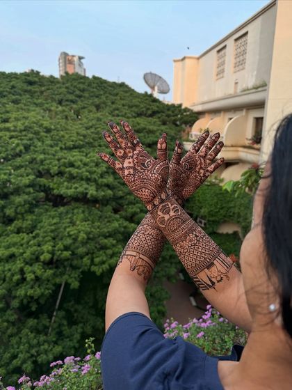 A bride showing off her intricate full-arm mehndi against a beautiful green backdrop.