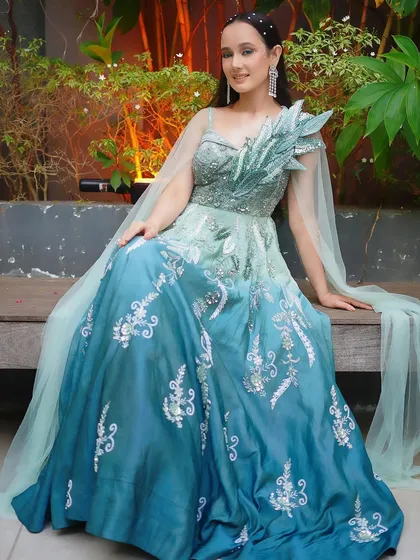 A stunning ombre gown that transitions from sea green to blue, with silver embroidery and a unique one-shoulder cape.