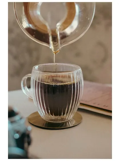 A pour-over coffee being decanted into a glass mug. This shot captures the process and craft of coffee making, appealing to cafe culture enthusiasts.