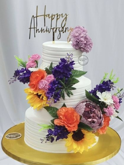 A vibrant three-tiered floral anniversary cake. We used a variety of colorful flowers like sunflowers, peonies, and lavender to create a lush, garden-like effect on this beautiful celebration cake.