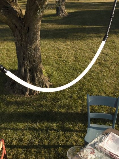 The Leda system used outdoors, hung from a tree to illuminate a rustic picnic table, showcasing its versatility and durability.