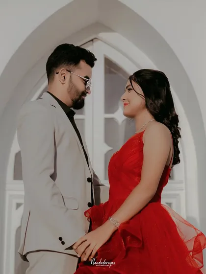 A classic couple's portrait in front of an arched white doorway, the bride's red dress providing a stunning pop of color.