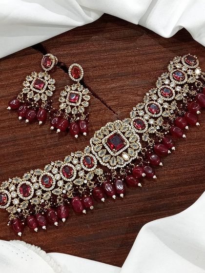 A versatile choker set available in multiple colors including white pearl, ruby, emerald, and pastel pink. The design features a central square motif with hanging beads, making it a popular choice for various festive occasions.