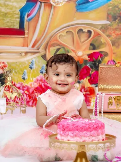 A joyful moment from a princess-themed cake smash, with the birthday girl smiling brightly in front of her carriage backdrop and pink cake.
