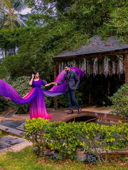 A couple with a flowing purple and pink gown on the wooden bridge, a vibrant and romantic image.
