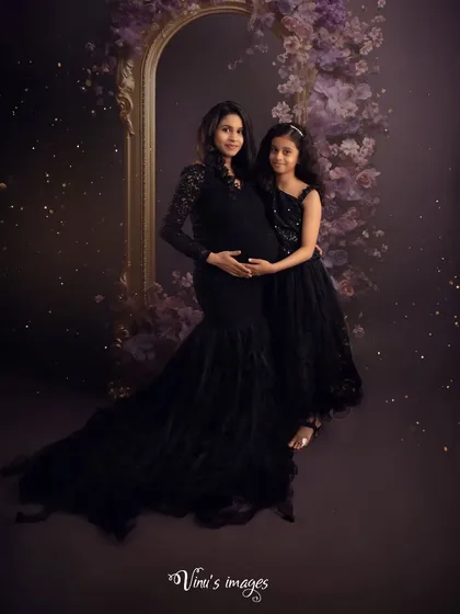 An elegant studio portrait of a mother and daughter. The coordinated black dresses and the soft, sparkling lights create a sophisticated and timeless image celebrating their bond before the new arrival.