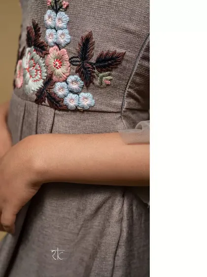A close-up of the intricate floral thread embroidery at the waist, which adds a beautiful pop of color and detail to the earthy brown dress.