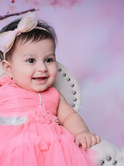 A beautiful close-up portrait of a smiling baby girl, framed by the soft pink hues of the cherry blossom backdrop.