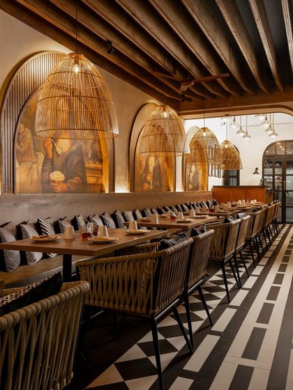 Long banquette seating under dramatic cane light fixtures and arched murals creates a cozy and communal dining atmosphere.