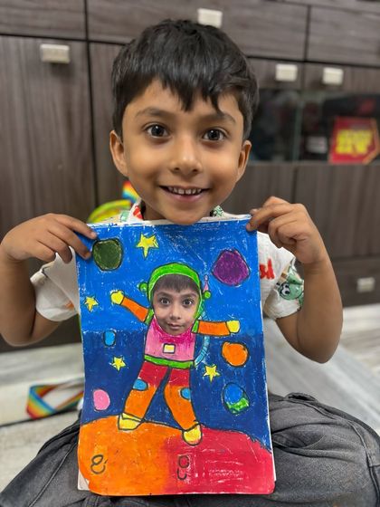 A young boy proudly holds his astronaut artwork, where his own face is part of the drawing. This fun craft project combines drawing, colouring, and personalization, making it a favourite among kids.