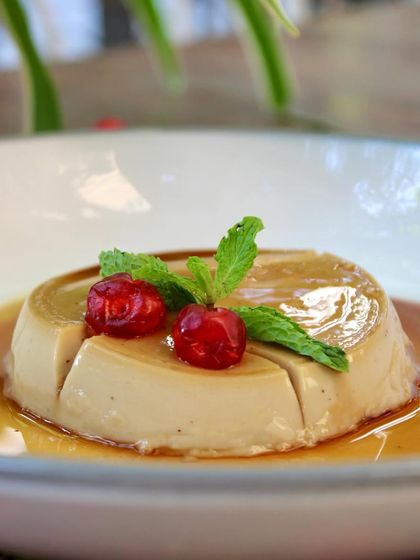 A perfect slice of our Vegan Caramel Pudding, garnished with fresh cherries and mint. It's a divine dessert that will satisfy your sweet cravings the compassionate way.