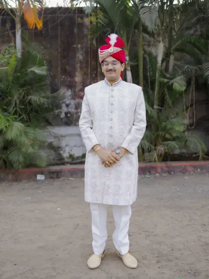A full-length portrait of the groom, showcasing his complete wedding outfit from the turban to the shoes.