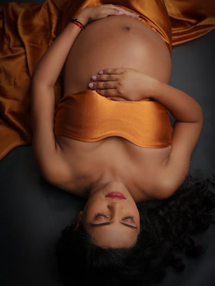 An artistic top-down shot focusing on the serene expression of the mom-to-be and her beautiful baby bump, draped in golden satin.