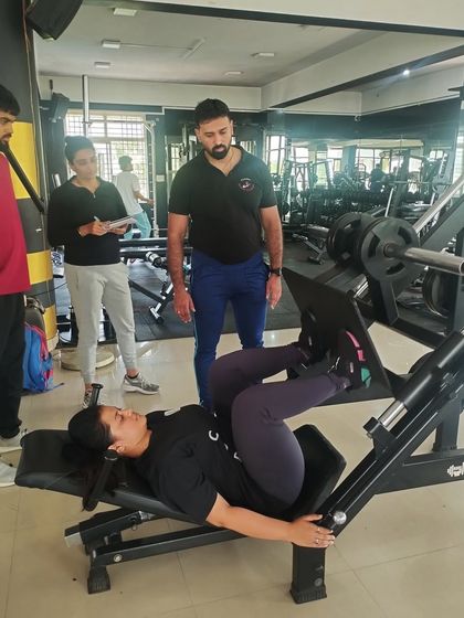 A student learns the correct use of a leg press machine under expert supervision, focusing on safety and muscle engagement.