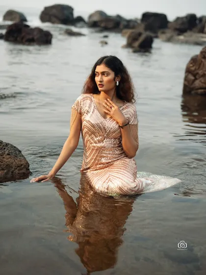 A thoughtful pose in a glamorous gown, with the model sitting in the water. The combination of the elegant dress and the natural ocean environment is both beautiful and unique.