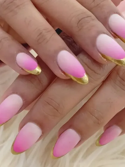 A unique ombré style with a matte pink gradient and striking gold chrome tips on almond-shaped nails.