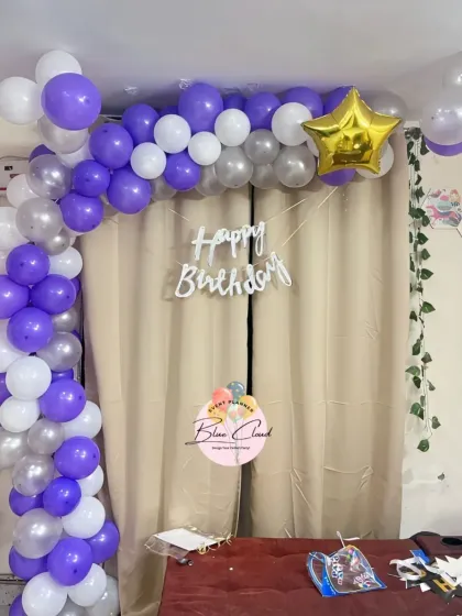A purple and silver balloon arch against a curtain for a simple birthday setup at home.