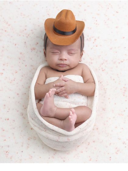 A little cowboy in a simple setup. The focus remains on the baby's adorable pose and tiny cowboy hat in this minimalist portrait.