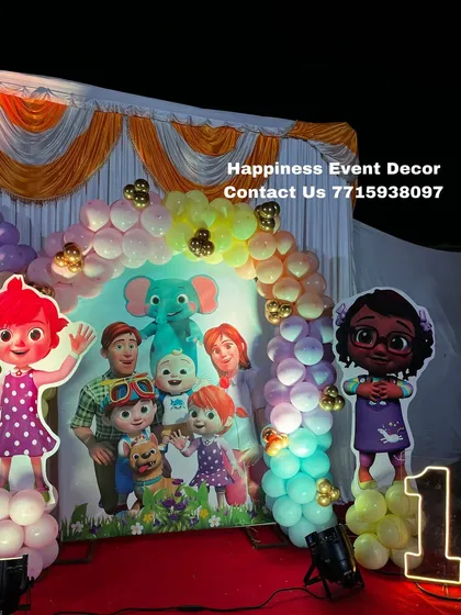 A Cocomelon theme setup for a first birthday, featuring character cutouts and a colorful balloon arch over a themed backdrop.